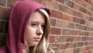 Sulky blonde teenage girl wearing a hoodie leaning against a wall, Billericay Essex UK
