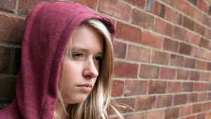 Sulky blonde teenage girl wearing a hoodie leaning against a wall, Billericay Essex UK